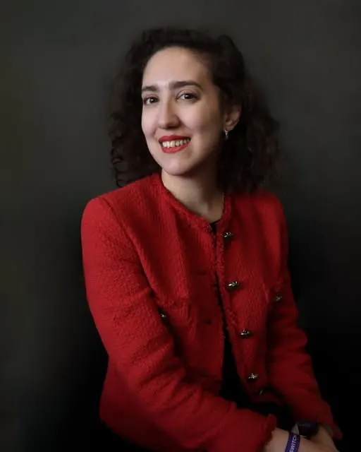 Retrato de Lucía sonriendo, con saco rojo, sobre fondo oscuro